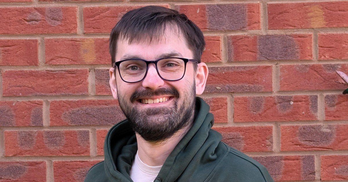 Conor Nicholson; A man with glasses and a beard is standing in front of a brick wall, smiling and wearing a green hoodie with "NICHOLSON VETERINARY CENTRE" written on it.